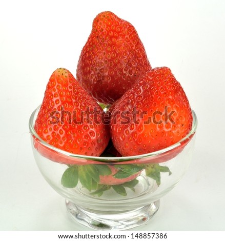 Strawberries in a glass bowl on a plain background.