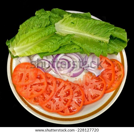 Lettuce tomato and onion on a plate on a black background.