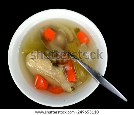 Chicken soup with chicken and a spoon on a black background.