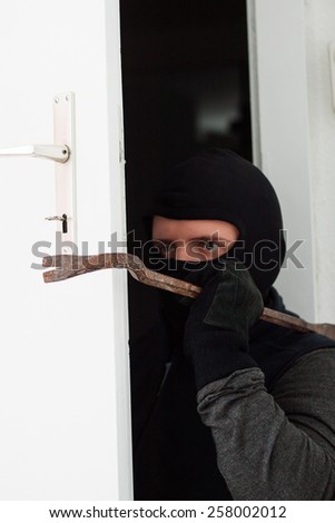 masked burglar breaking the door with crowbar