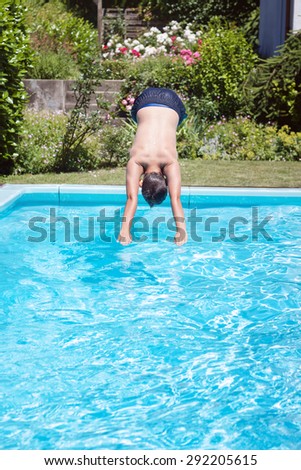 young boy jumping into the pool in front of green plants
