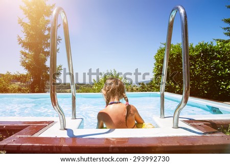 back of young girl sitting on poolside at garden in summertime