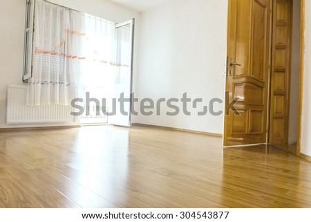 empty room with white walls and wooden laminate and open wooden door