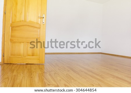 empty room with white walls and wooden laminate and open wooden door