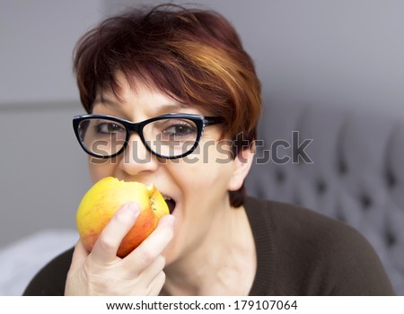 portrait of mature woman in black glasses eating an apple