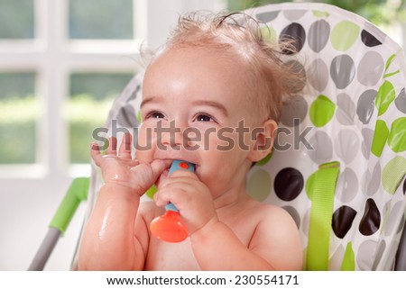 Funny smiling ragged baby putting spoon in to mouth