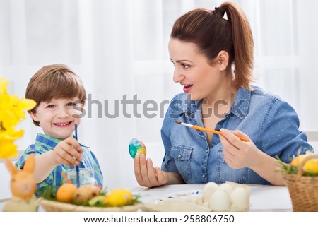 Loving young mother and her child painting easter eggs