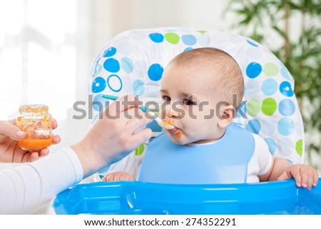Cute hungry baby eating fruit mash in the kitchen