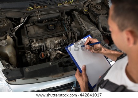 Mechanic checking list of car parts on clipboard