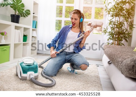 Smiling excited young housewife havig fun with vacuum cleaner