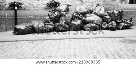 Pile of garbage sitting beside a cobblestone street in black and white