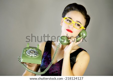 Closeup of a beautiful young girl with yellow glasses holding an old green rotary phone