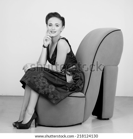 Beautiful Brunette in a dress sitting on a chair shaped in a shoe in black and white