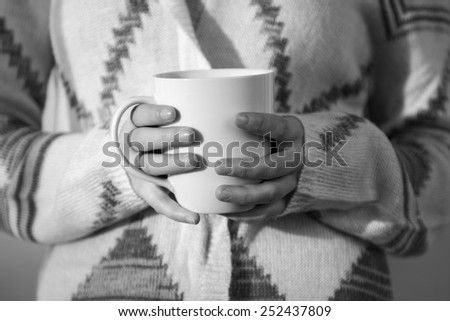 Close up of a white coffee mug being held by a young woman in black and white