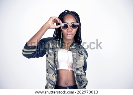 Beautiful black woman posing in a studio wearing a white tube top, camo jacket, heels and jeans.