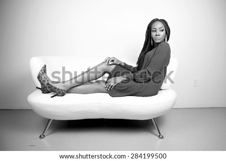Beautiful fashion model in a teal dress on a white couch in black and white