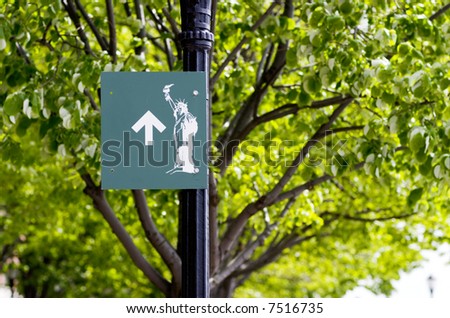Green sign on a lamppost showing the direction to the Statue of Liberty