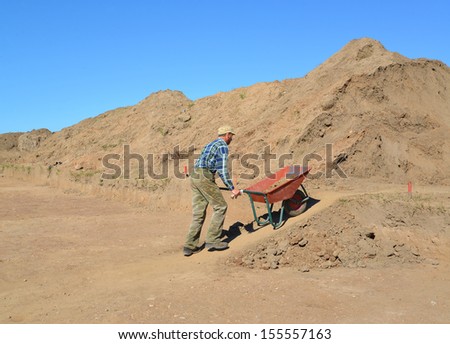 The man of average years is lucky a wheelbarrow with soil on road construction