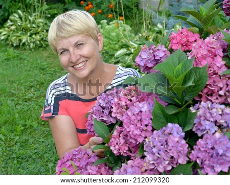 The happy woman of average years near a blossoming hydrangea in a garden