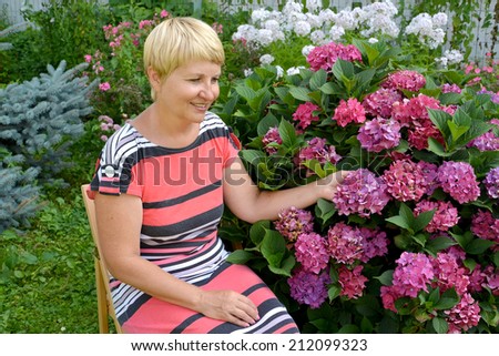 The joyful woman of average years has a rest in a garden near a blossoming hydrangea