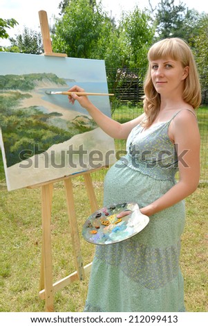 The young pregnant female artist writes a picture with oil paints