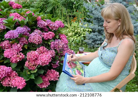 The young pregnant female artist draws water color paints a blossoming hydrangea in a garden