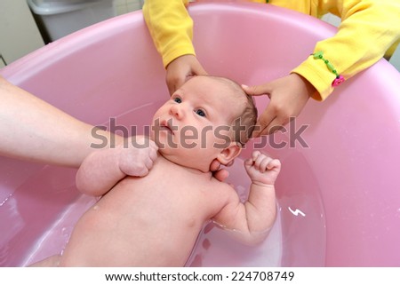 The little girl helps mother to bathe the baby