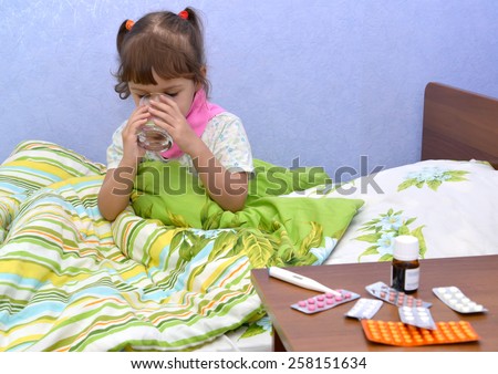 The little sick girl sits in a bed and drinks water from a glass. Treatment