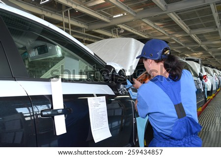KALININGRAD, RUSSIA - SEPTEMBER 16, 2014: The female collector fixes a mirror on a car body by means of the screw gun. Assembly conveyor of automobile plant