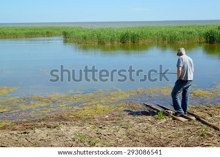 KALININGRAD, RUSSIA - JUNE 06, 2015: An old man catches fish a rod in a creek of the Baltic Sea