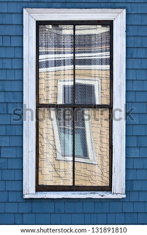 Window Reflections: Window in a blue wooden shingled house reflects the window of a yellow wooden shingled house across the street.