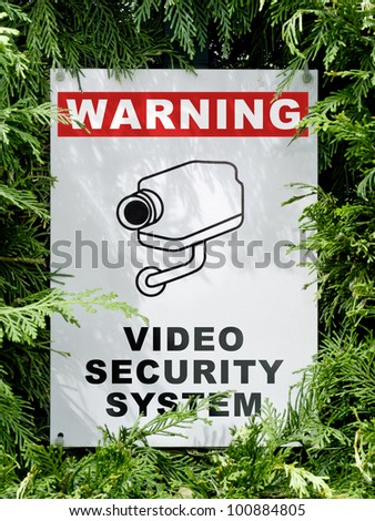video security system warning signboard on a fence hedge