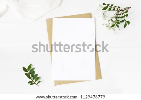 Feminine wedding stationery, desktop mock-up scene. Blank greeting card, craft envelope, baby\'s breath flowers, silk ribbon and lentisk branches. Old white wooden table background. Flat lay, top view.