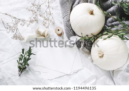 Autumn styled photo. Feminine wedding desktop stationery mockup scene with blank greeting card, eucalyptus, ribbons, white pumpkins and gypsophila flowers. Table background. Thanksgiving. Flat lay.
