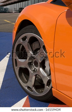 expensive orange super car front tire with office in background