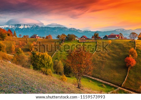 Beautiful autumn alpine landscape, famous alpine village with stunning colorful clouds and high snowy mountains in background near Bran, Magura village, Transylvania, Romania, Europe