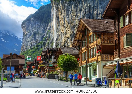 Spectacular principal street of Lauterbrunnen with shops,hotels,terraces,swiss flags and stunning Staubbach waterfall in background,Bernese Oberland,Switzerland,Europe