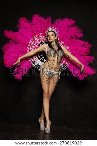 Beautiful woman in crown and carnival dress with feathers on black background