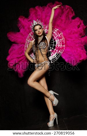 Beautiful woman in crown and carnival dress with feathers on black background