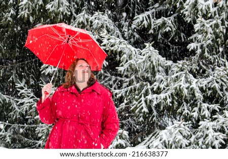 A woman in a red coat with a red umbrella enjoys a walk on a snowy white day