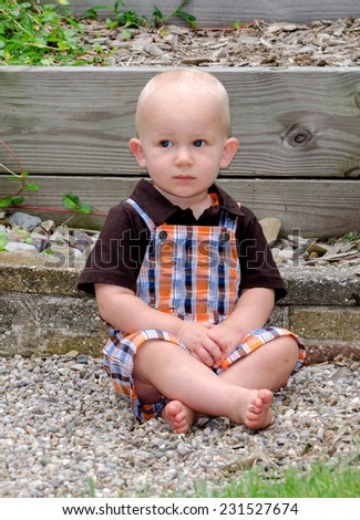 adorable blond toddler  sitting on a rocky step in a back yard garden