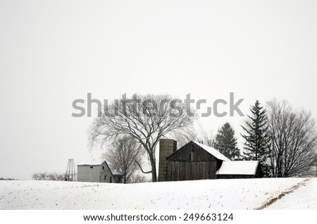 A rustic winter farm house and barn make a monochromatic landscape