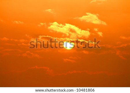 Beautiful orange sun covered by small clouds.