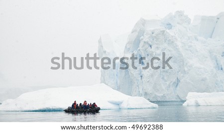 A zodiac boat filled with people looking at a massive iceberg in a snow storm - Antarctica