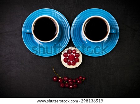 A smiley face arranged of two cups of coffee, cake and red currant