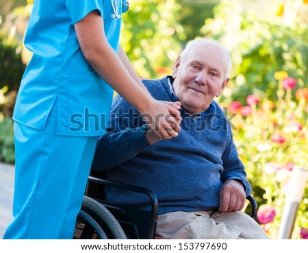 Old patient sitting in wheelchair, holding the doctor\'s hand.