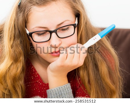 Close-up of a confused teenage girl holding  a positive pregnancy test.