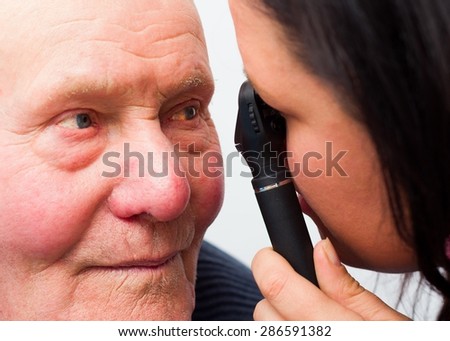 Optician checking elderly patient\'s cataracts with optical device.
