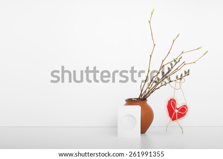 Soft spring background. Romantic gift card, with clay vase full of fresh branches and plush red heart on background. Vintage interior