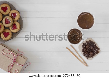 Two cups of just brewed coffee with plate of cookies in shape of hearts and carton gift box on white wooden table vintage retro background